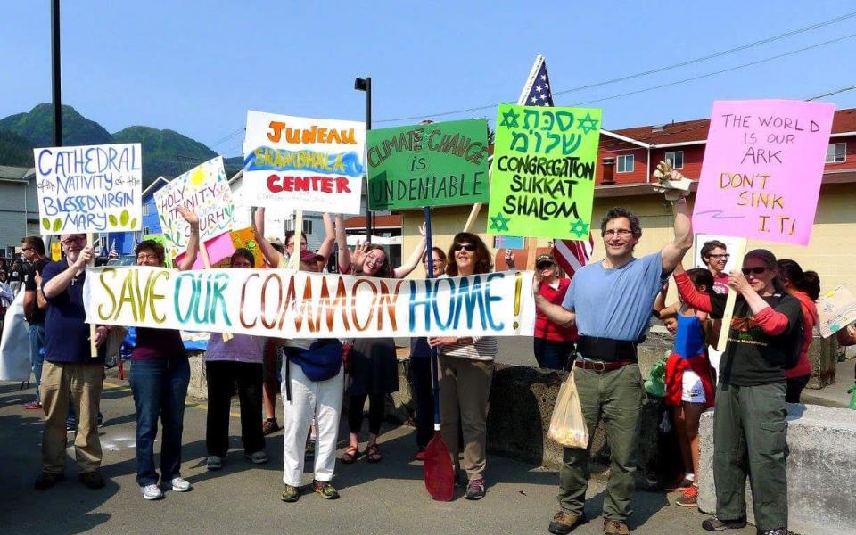 Alaska Interfaith Power and Light members hold banner and signs.